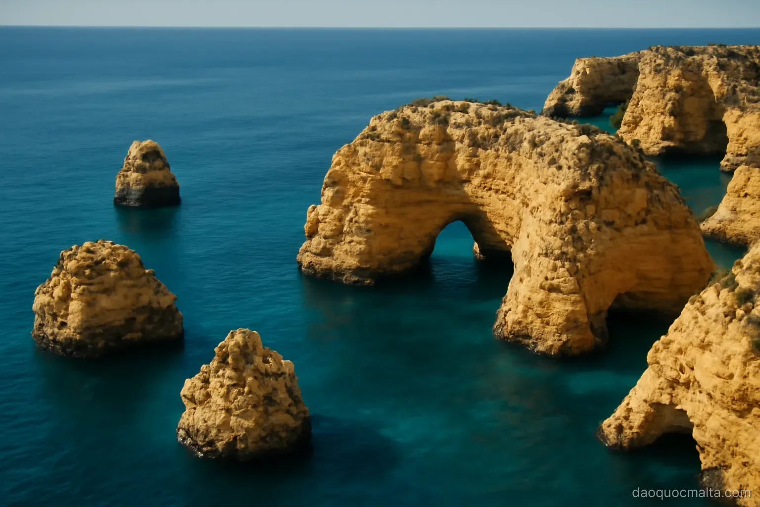 an aerial view of a small limestone archipelago with deep blue sea around golden cliffs