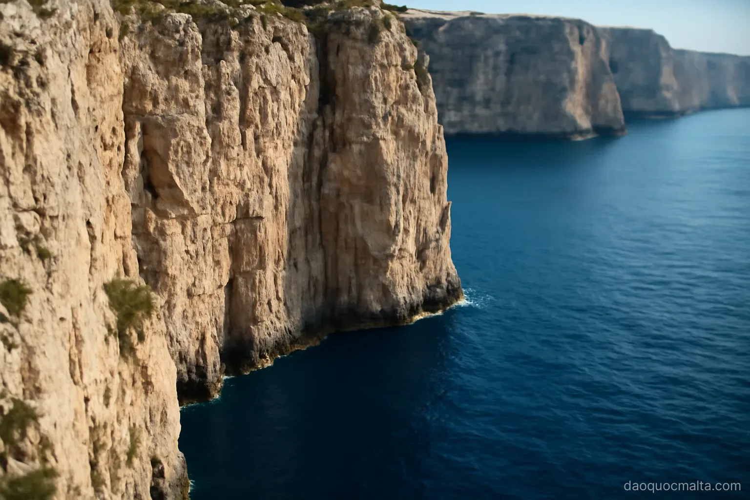 sheer limestone cliffs dropping straight into deep blue sea with no beach below